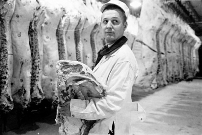 Butcher holding slab of beef in a meat locker.